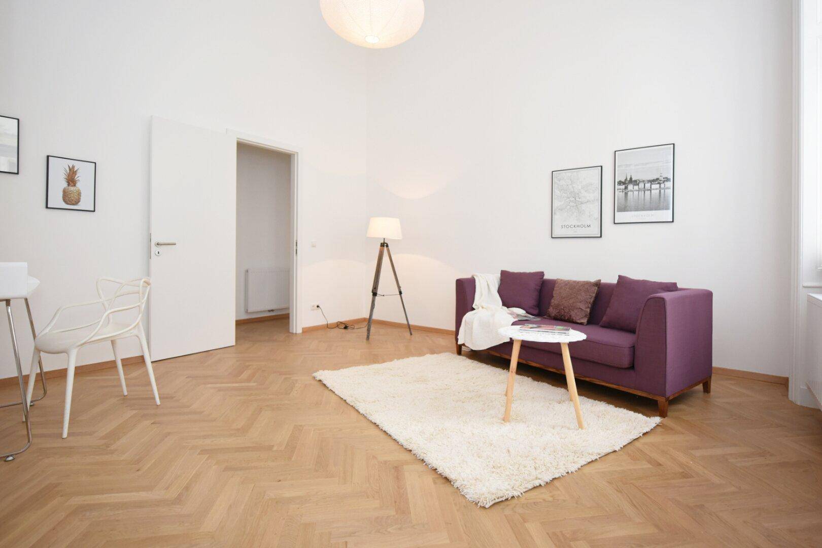 Helles Wohnzimmer mit Fischgrätparkett, modernem Sofa und minimalistischer Einrichtung.