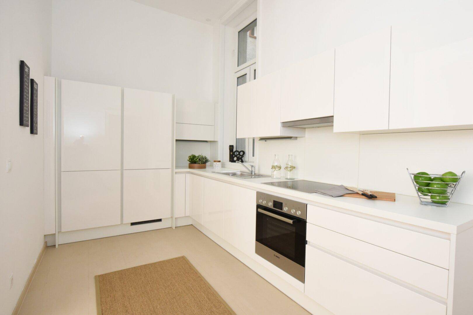 Moderne weiße Küche mit Hochglanzfronten, Einbaugeräten und Fenster.