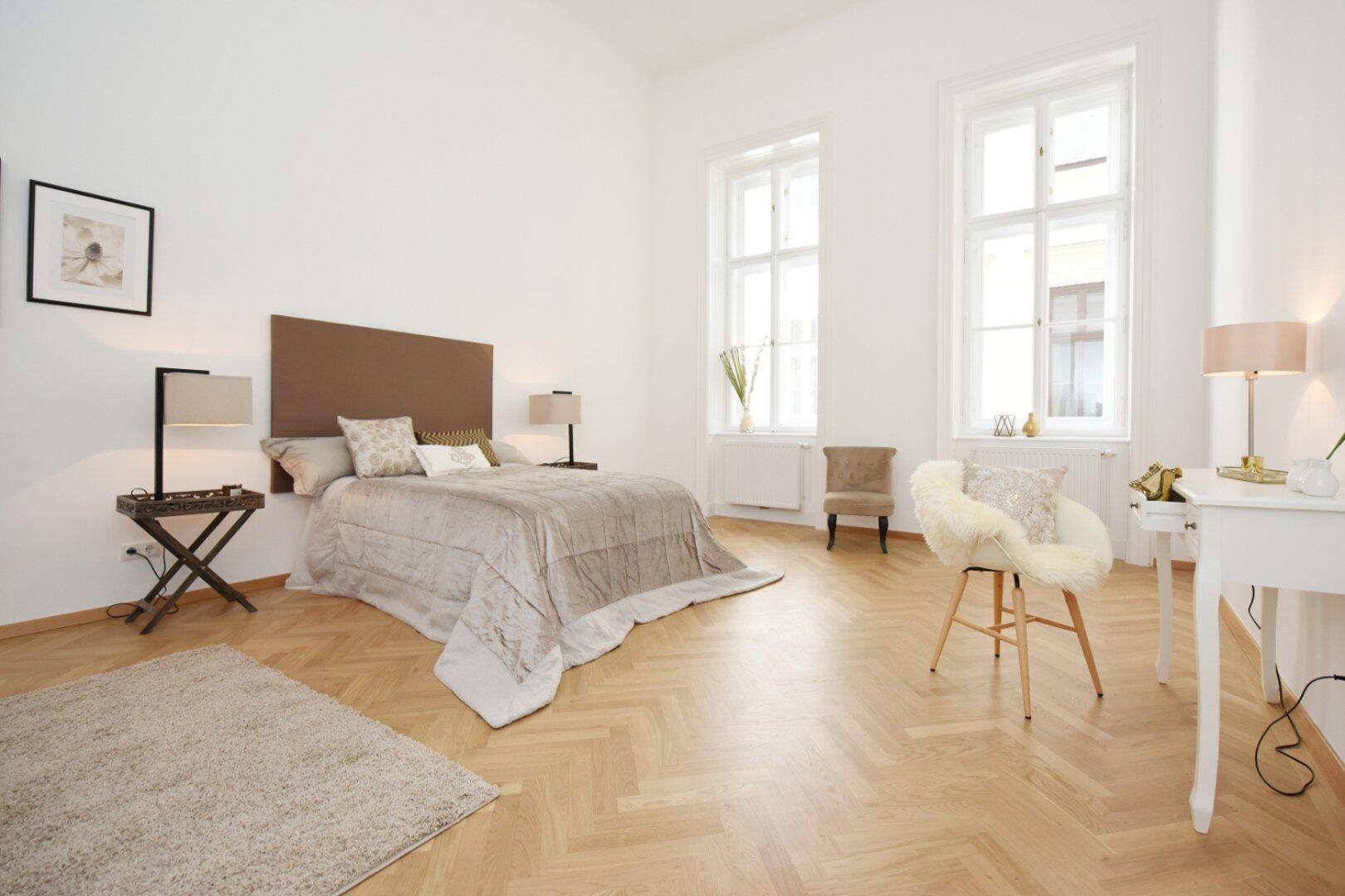 Helles Schlafzimmer mit Fischgrätparkett, hohen Fenstern und modernem Bett.