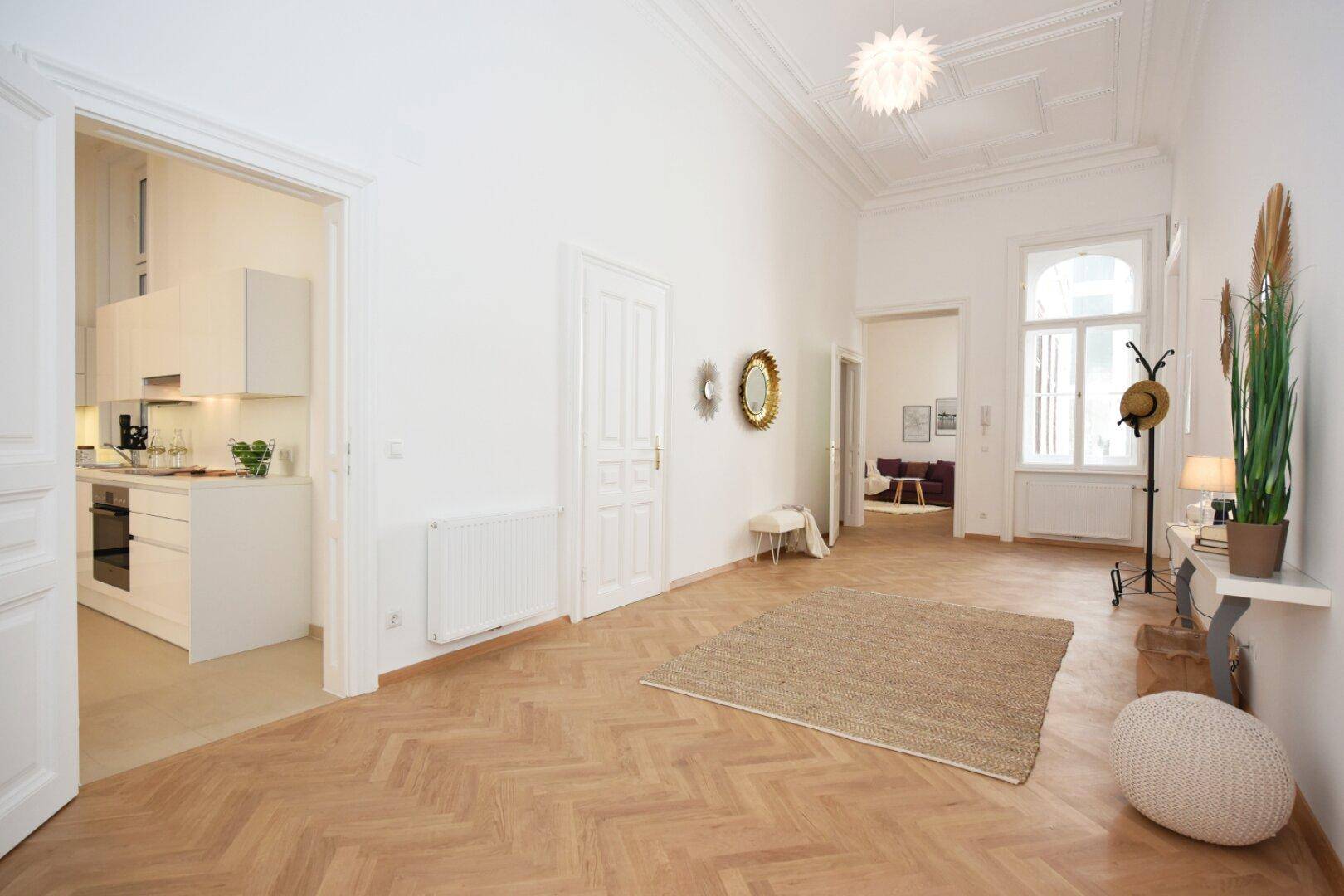 Geräumiger Flur mit Fischgrätparkett, hohen Decken und Zugang zur modernen Küche.