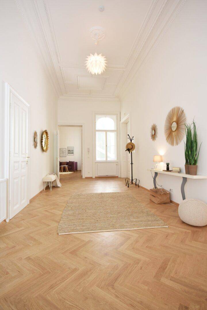Langer, heller Flur mit Fischgrätparkett, hohen Decken und dekorativen Elementen.