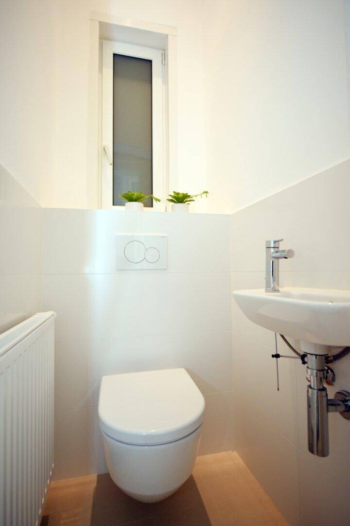 Modernes Gäste-WC mit wandhängender Toilette, kleinem Waschbecken und Fenster.
