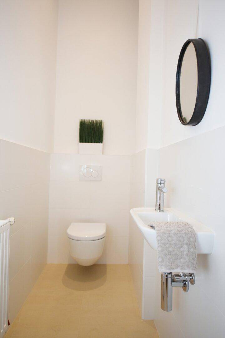 Helles Gäste-WC mit wandhängender Toilette, kleinem Waschbecken und Spiegel.