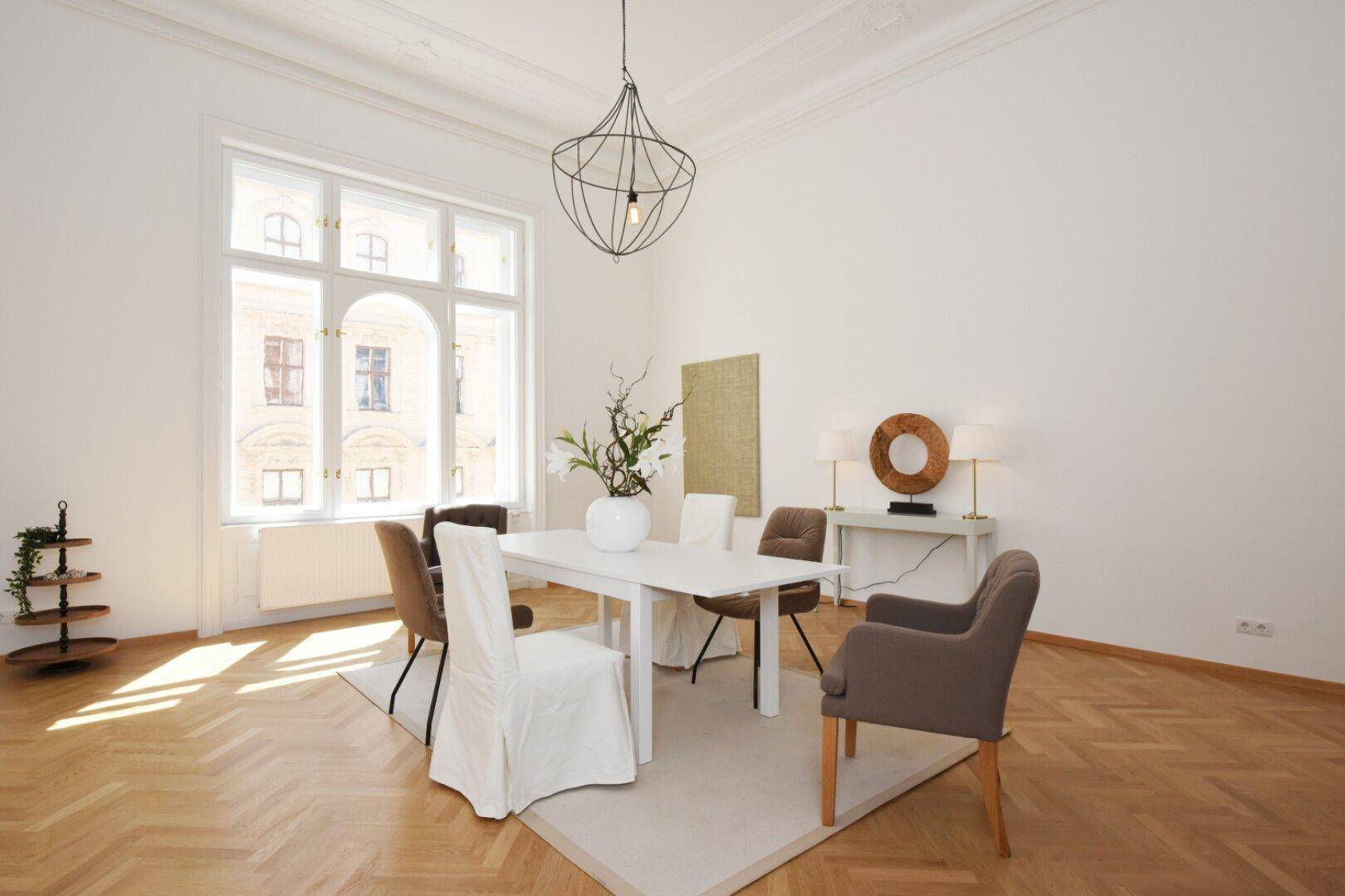 Lichtdurchfluteter Essbereich mit Fischgrätparkett, modernem Kronleuchter und großen Fenstern.
