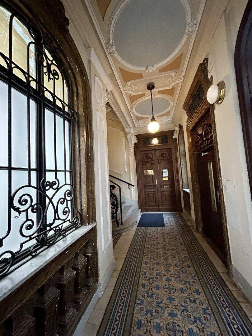 Historischer Flur mit Stuckdecke, verzierten Fenstern und gemustertem Fliesenboden in einem Altbau.