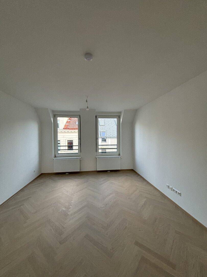 Unmöbliertes Schlafzimmer mit Fischgrätparkett und Blick auf die umliegenden Gebäude.