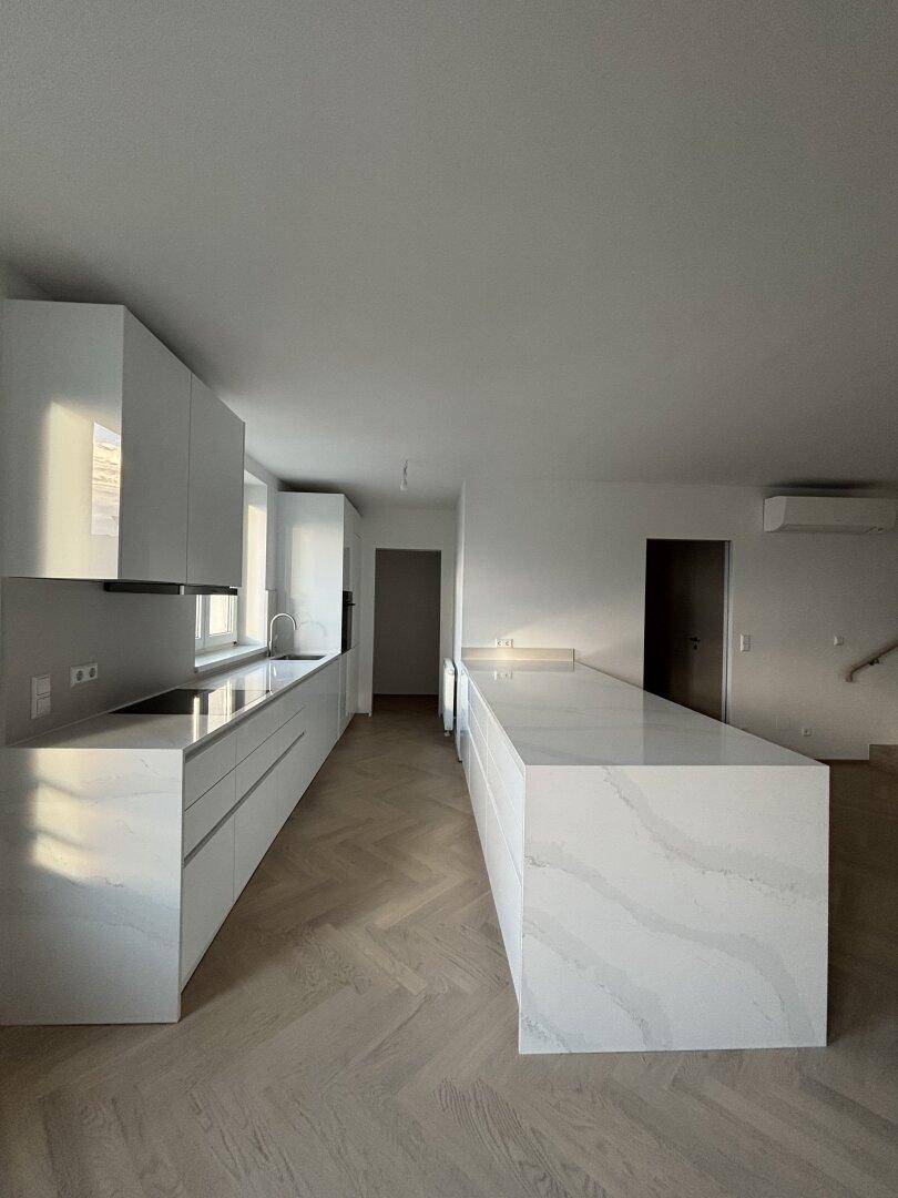 Moderne, unmöblierte Küche mit weißer Küchenzeile, Insel und Fischgrätparkettboden.