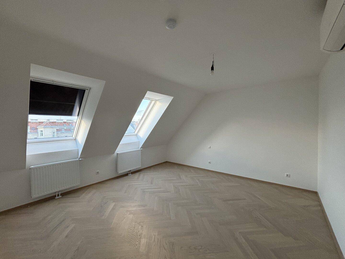 Helles Schlafzimmer im Dachgeschoss mit schrägen Wänden, Dachfenstern und Parkettboden.