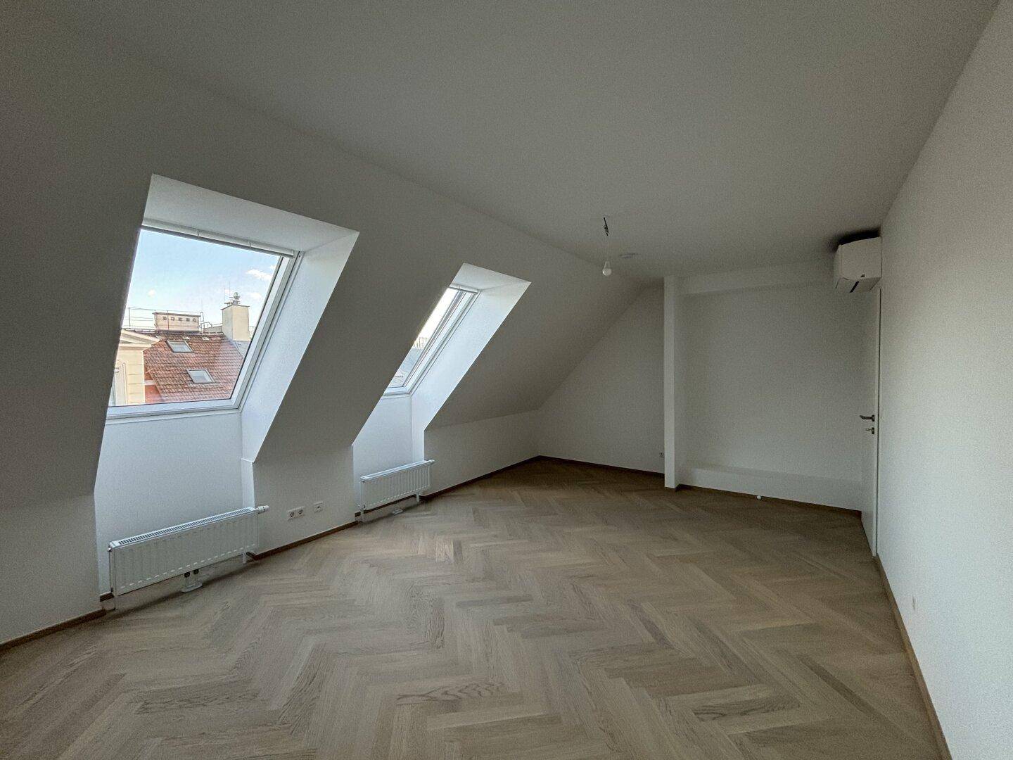 Lichtdurchflutetes Dachgeschosszimmer mit schrägen Wänden, Dachfenstern und Parkettboden.
