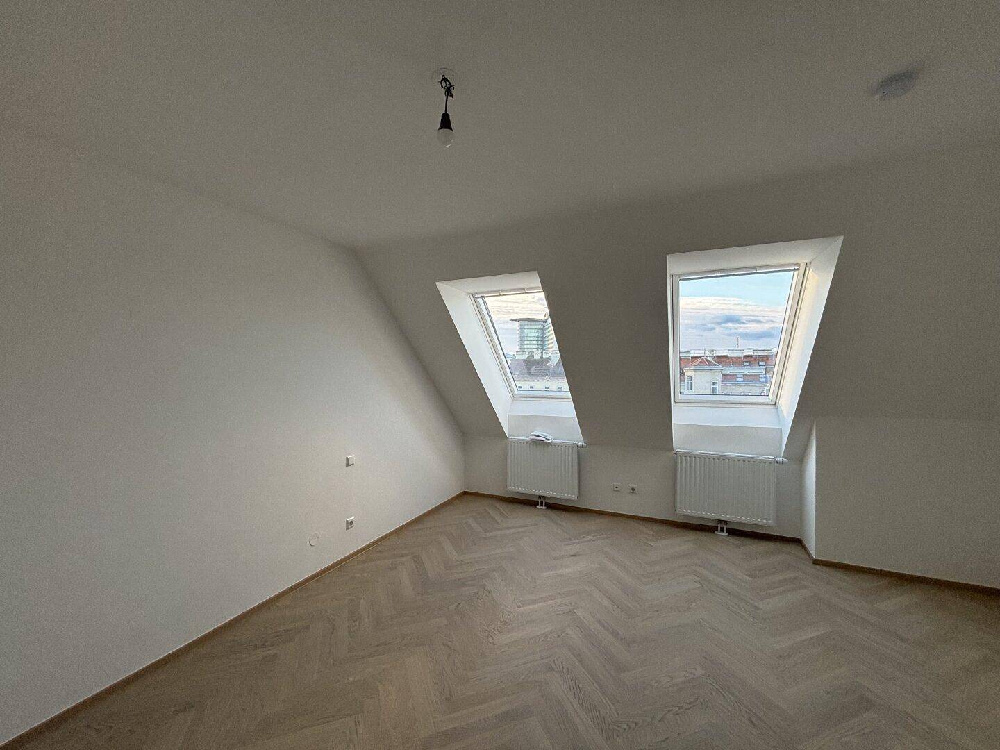 Geräumiges Dachgeschosszimmer mit zwei Dachfenstern, schrägen Wänden und Parkettboden.