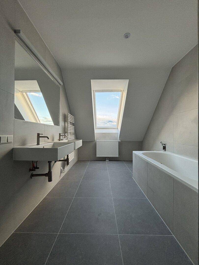 Modernes Badezimmer mit Doppelwaschbecken, Badewanne, grauen Fliesen und Dachfenster.