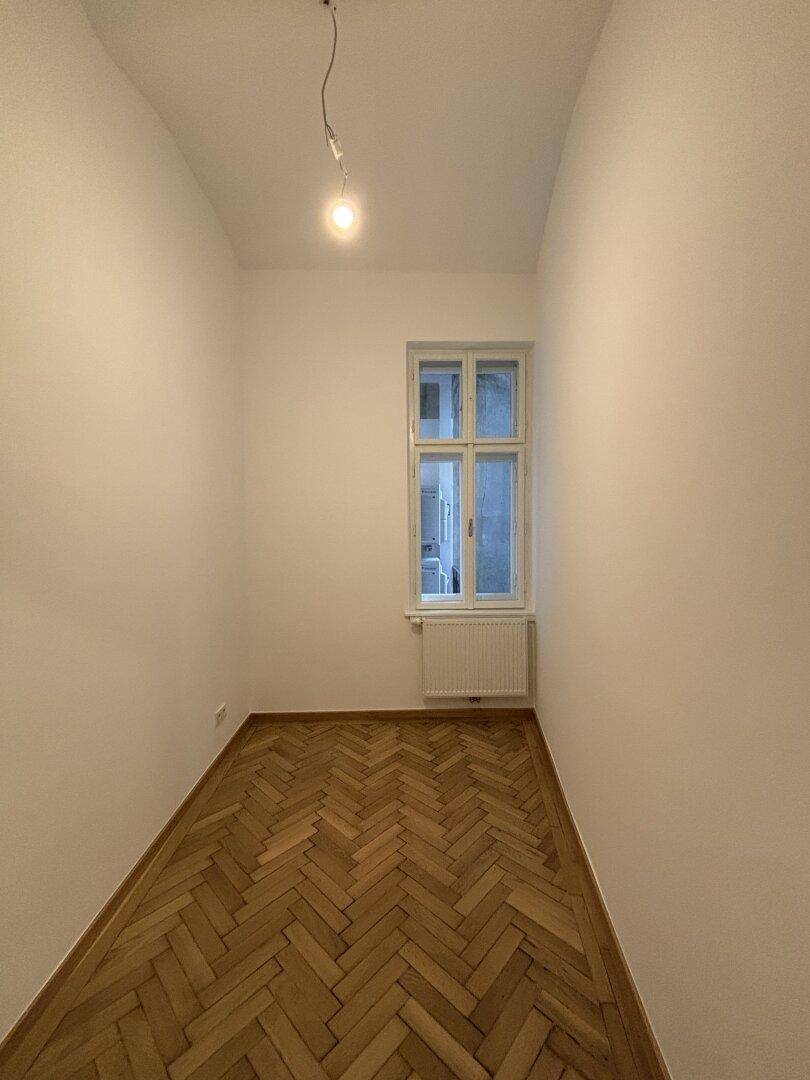 Schmaler, heller Raum mit Fischgrätparkett und Fenster, ideal als kleines Büro oder Abstellraum.