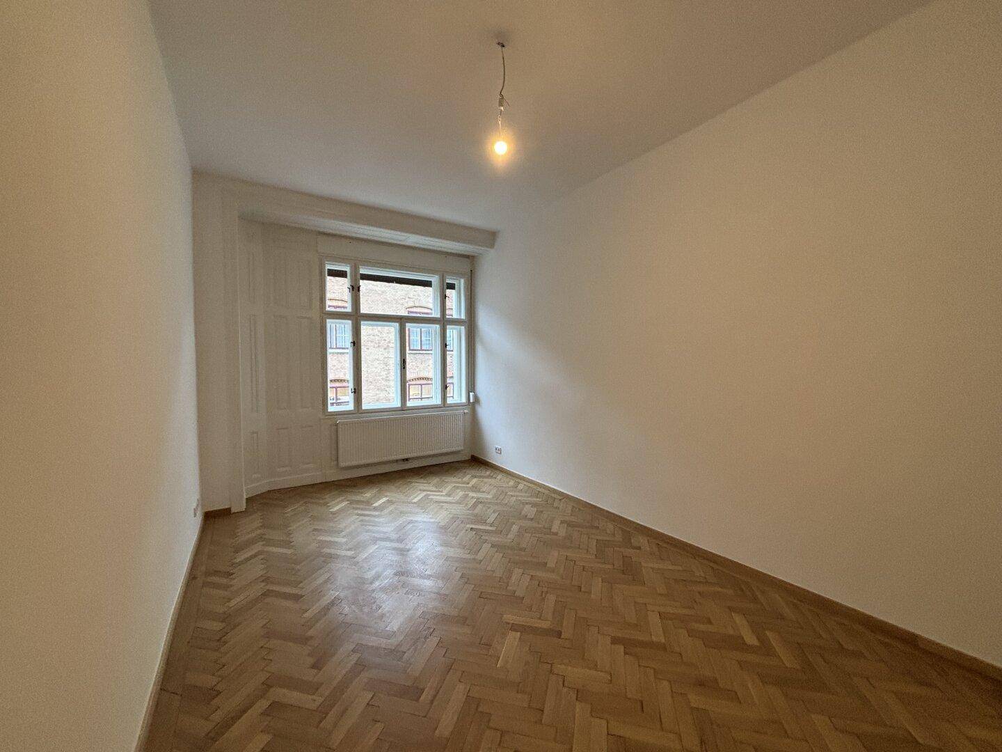Heller Raum mit Fischgrätparkett und großem Fenster, bietet eine angenehme Atmosphäre.