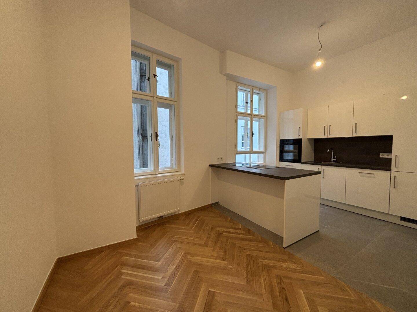 Heller Küchenbereich mit modernen weißen Schränken, einer Kücheninsel und zwei Fenstern.