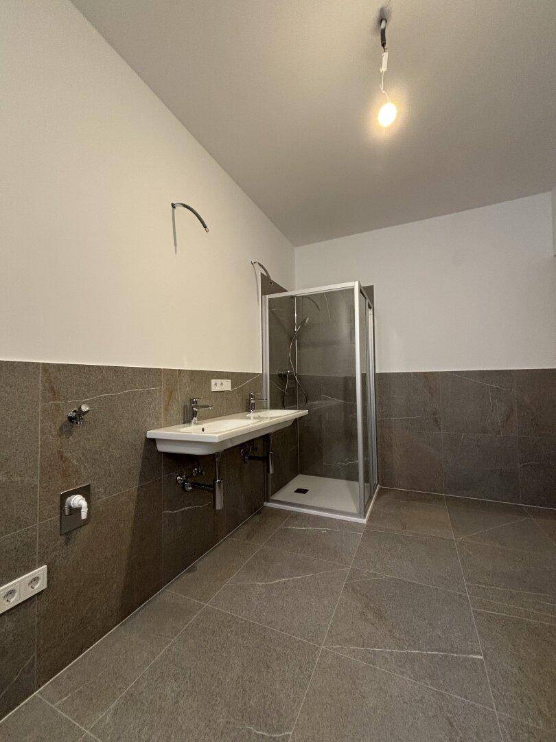 Modernes Badezimmer mit Duschkabine, Doppelwaschbecken und eleganten grauen Fliesen.