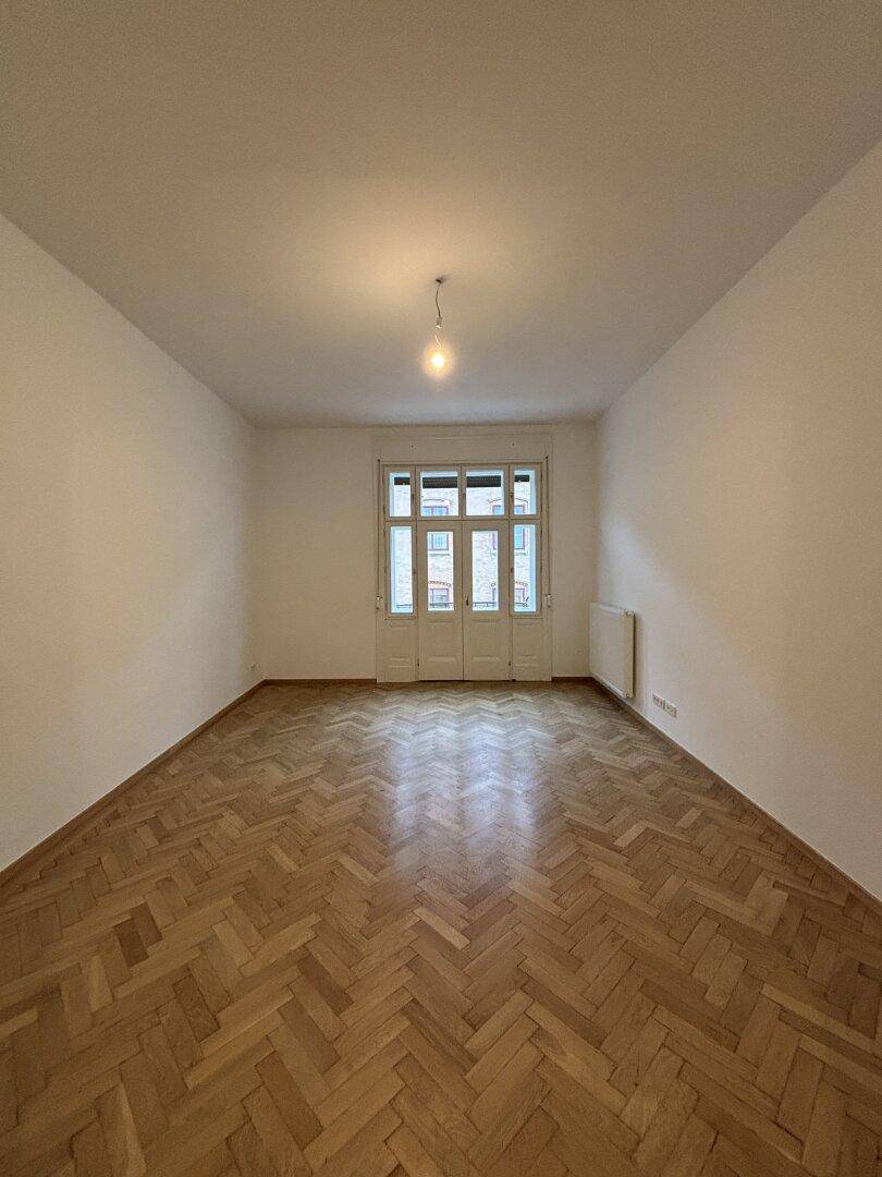 Weitläufiger, unmöblierter Raum mit elegantem Fischgrätparkett und Balkontür, bietet viel Gestaltungsfreiheit.
