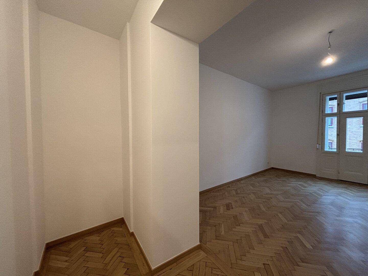 Ecke eines Raumes mit Fischgrätparkett, die den Übergang zu einem weiteren Bereich andeutet.