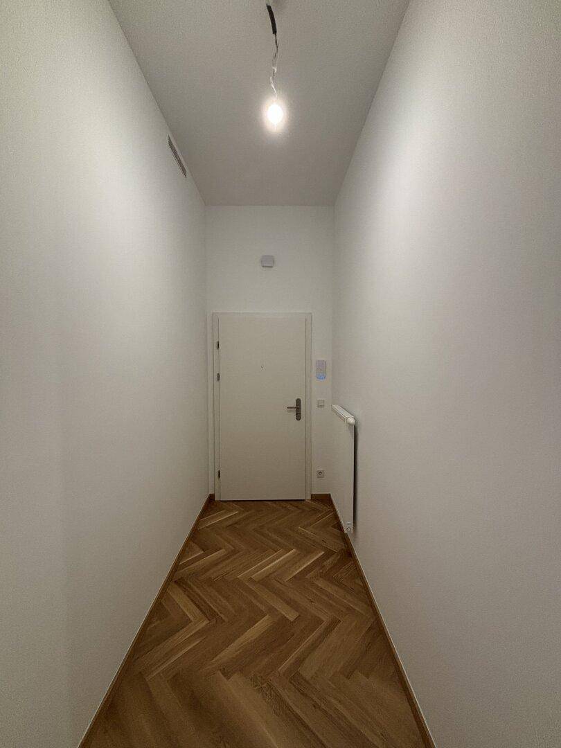 Heller Eingangsbereich mit Fischgrätparkett und weißer Eingangstür, der in die Wohnung führt.