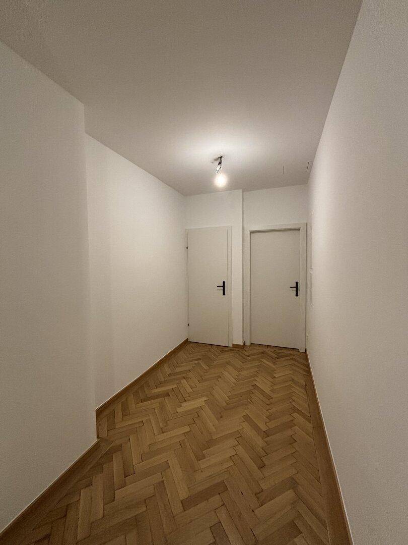Heller Flur mit Fischgrätparkett und zwei weißen Türen, der die verschiedenen Räume verbindet.
