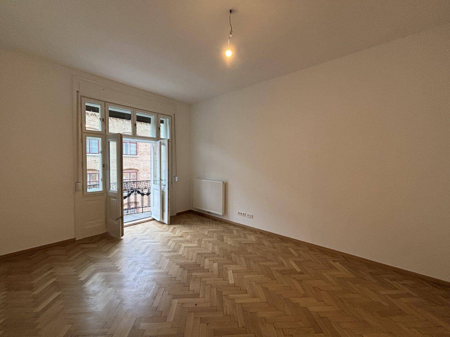 Geräumiger, leerer Raum mit Fischgrätparkett und Zugang zu einem Balkon, bereit zur individuellen Gestaltung.