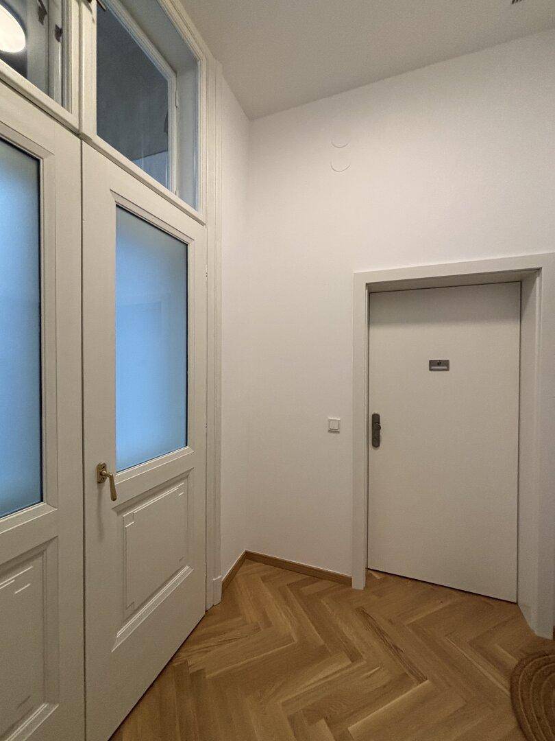 Flur mit Fischgrätparkett und Türen, darunter eine mit Milchglas, die für Privatsphäre sorgt.