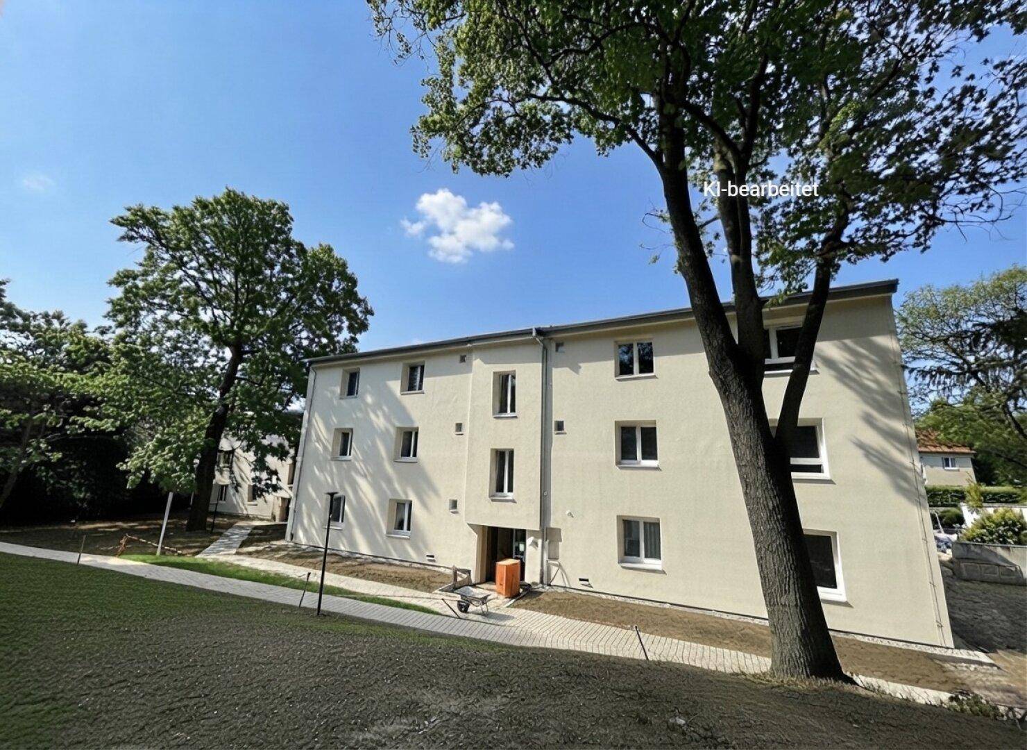Modernes Mehrfamilienhaus mit heller Fassade und vielen Fenstern, umgeben von Bäumen und Grünflächen.