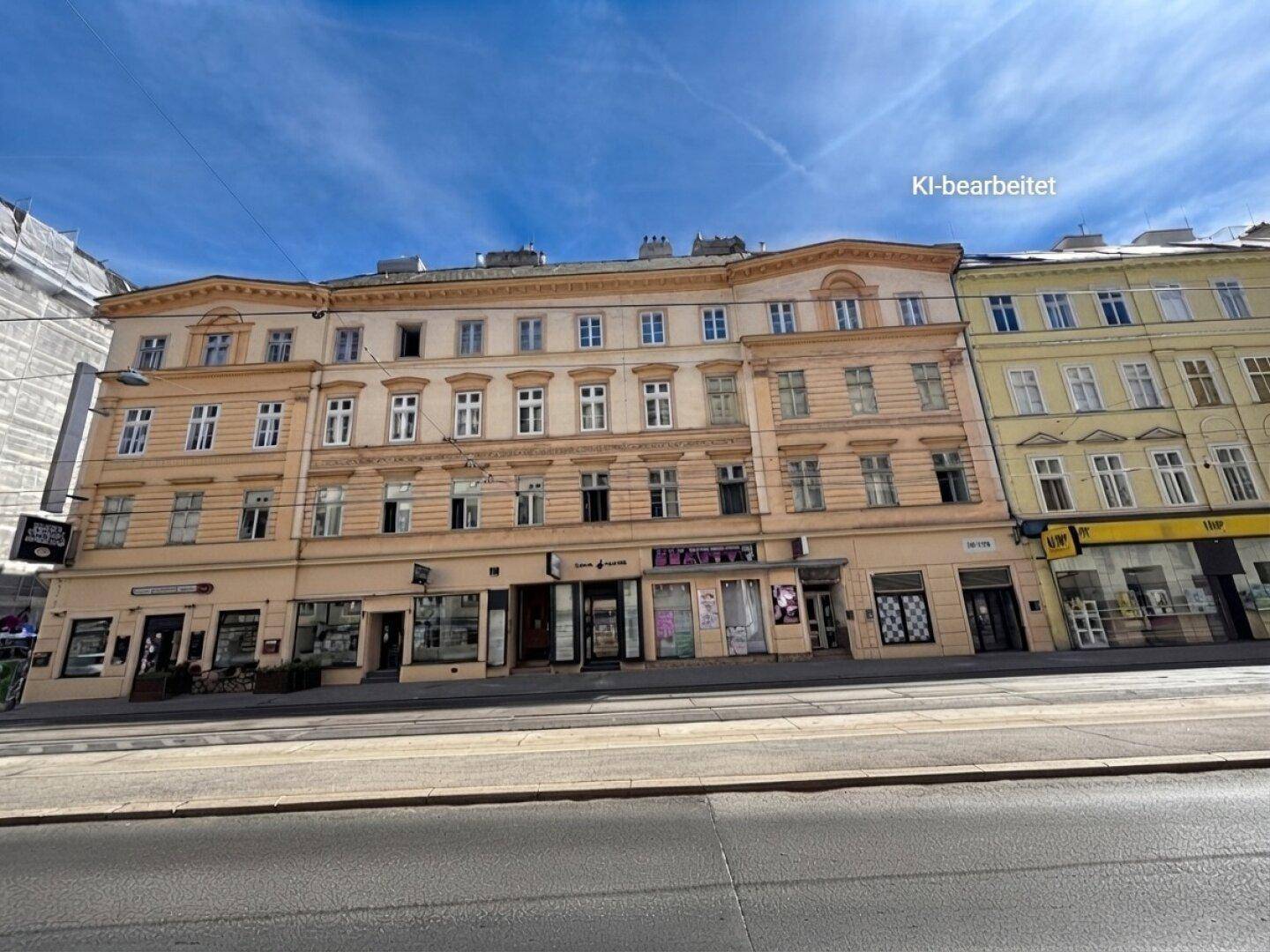 Historische Fassade eines Mehrfamilienhauses mit Geschäften im Erdgeschoss an einer Straße.
