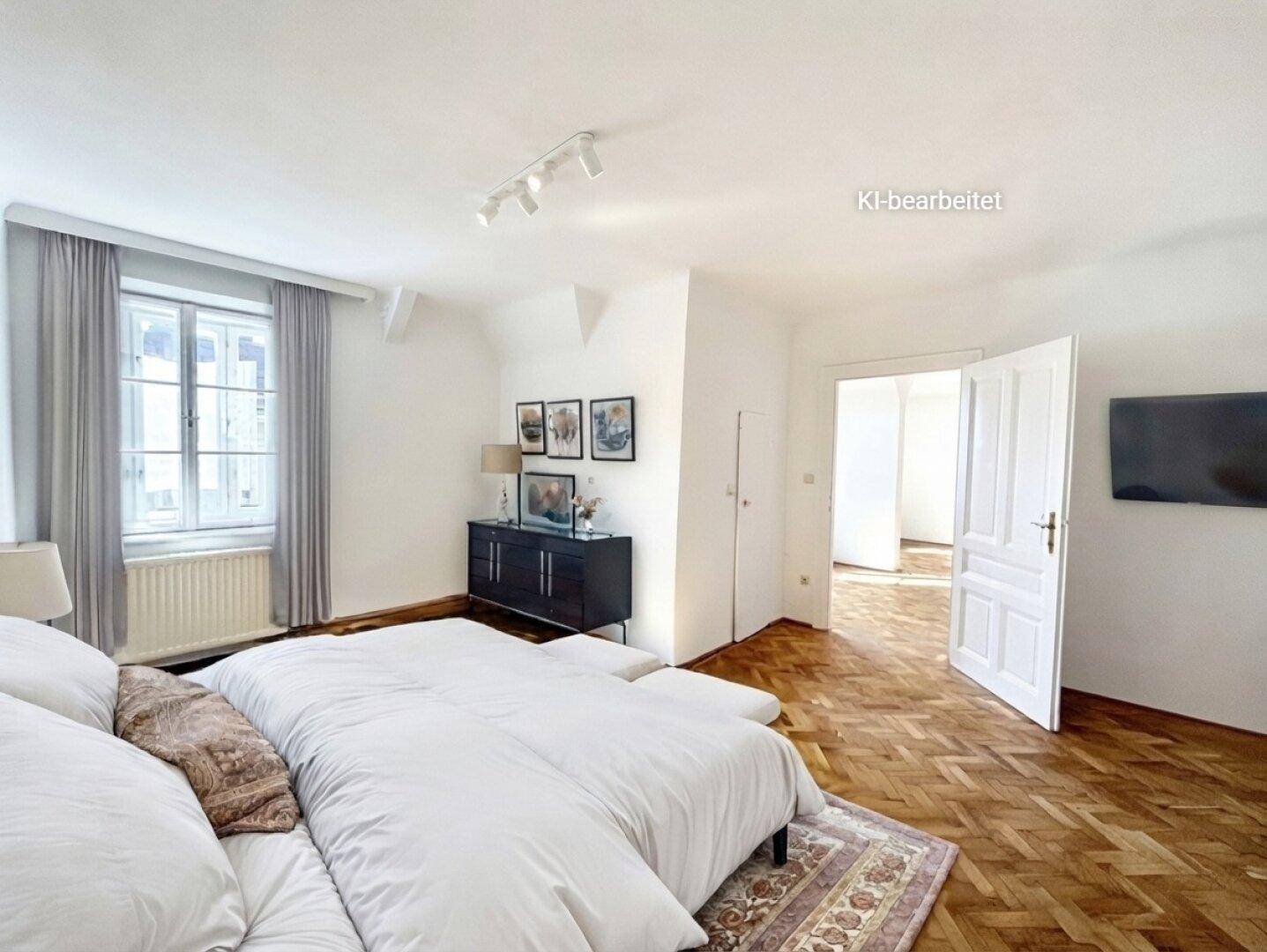 Geräumiges Schlafzimmer mit hellem Fischgrätparkett, großem Bett und natürlichem Lichteinfall durch das Fenster.