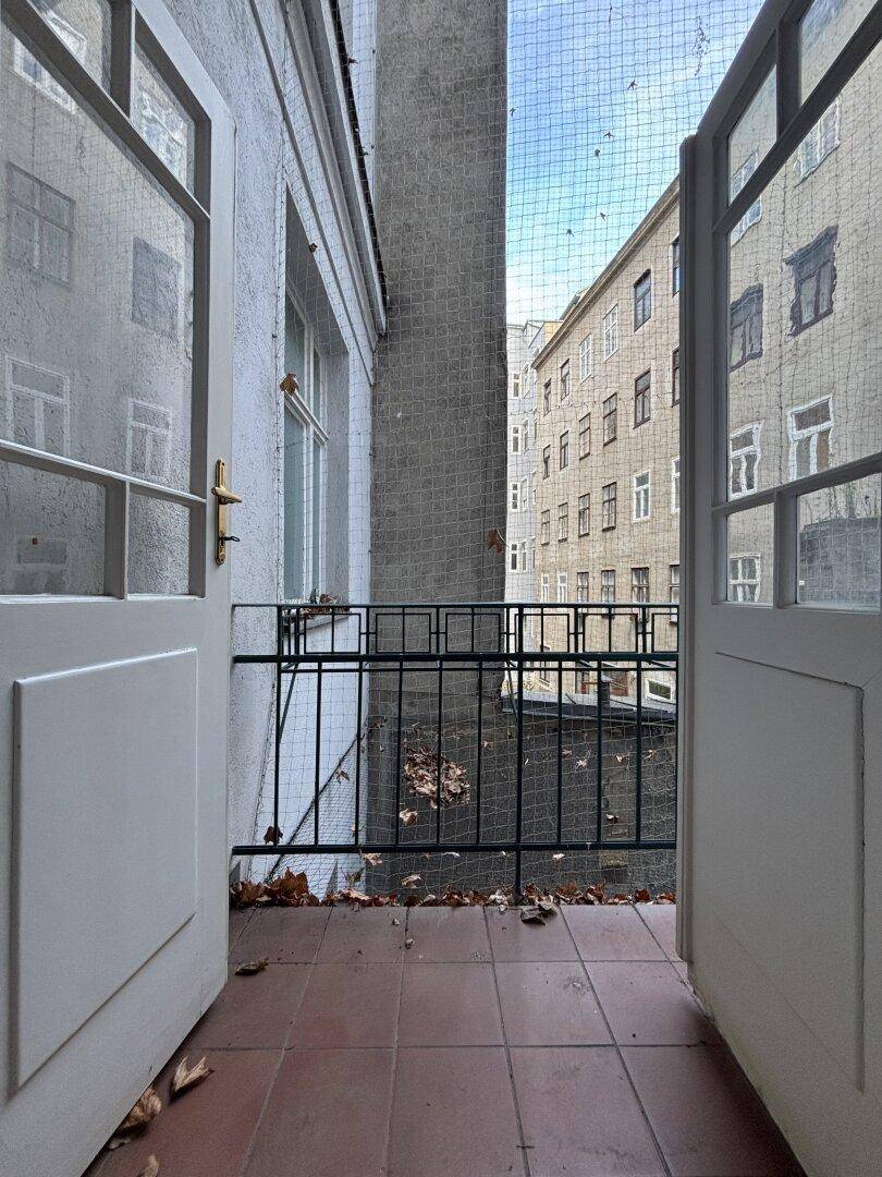 Kleiner Balkon mit Terrakottafliesen und schmiedeeisernem Geländer, umgeben von historischen Stadtgebäuden.