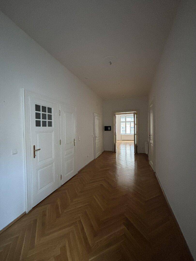 Heller Flur mit elegantem Fischgrätparkett und weißen Wänden, der die verschiedenen Wohnbereiche verbindet.