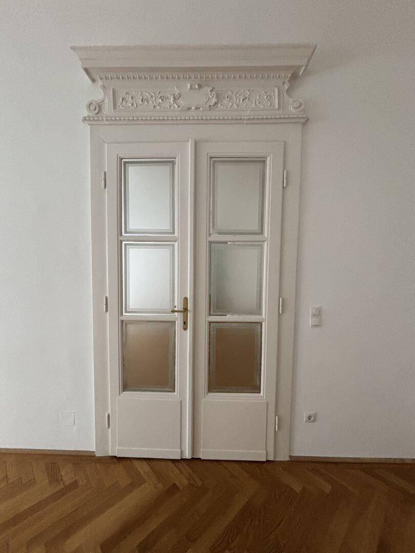 Detailaufnahme einer eleganten Doppeltür mit Zierrahmen und Milchglas, die den Altbaucharme unterstreicht.