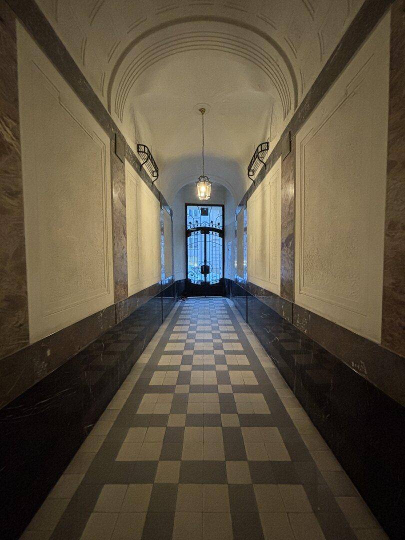 Eleganter Eingangsbereich mit Gewölbedecke, Schachbrettmuster-Fliesenboden und Marmorverkleidung, typisch Altbau.