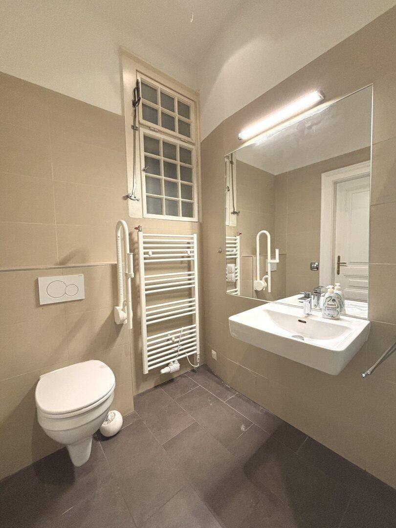 Modernes Badezimmer mit beigen Fliesen, wandhängendem WC, Einzelwaschbecken und beheiztem Handtuchhalter.