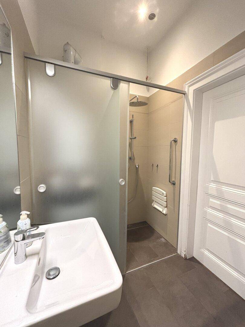 Barrierefreies Badezimmer mit begehbarer Dusche, Einzelwaschbecken und Haltegriffen für Komfort und Sicherheit.