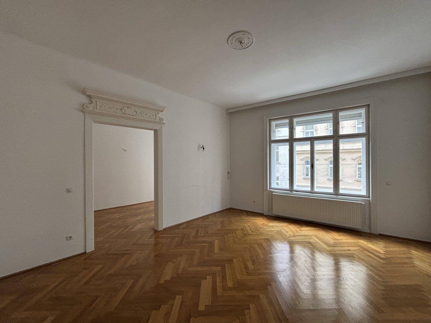 Geräumiges, leeres Wohnzimmer mit klassischem Fischgrätparkett und Stuckdecke, bereit zur individuellen Gestaltung.
