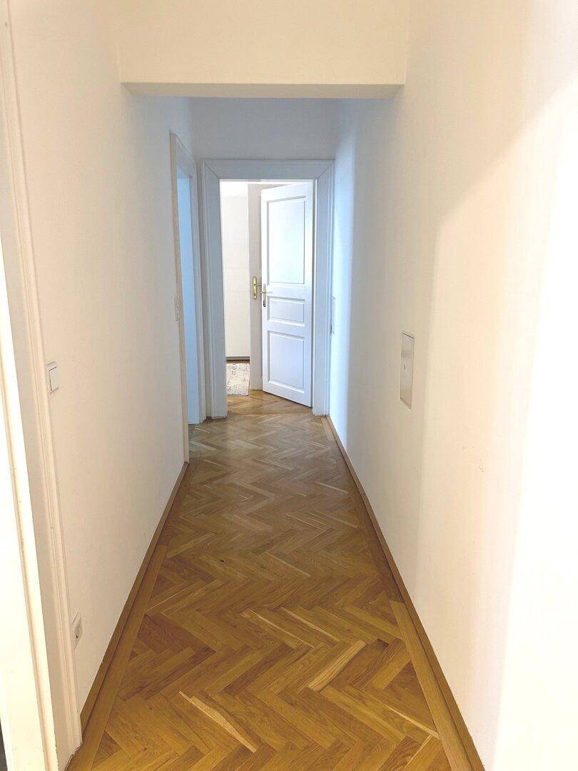 Langer Flur mit Fischgrätparkett und weißen Wänden, der zu weiteren Räumen führt.