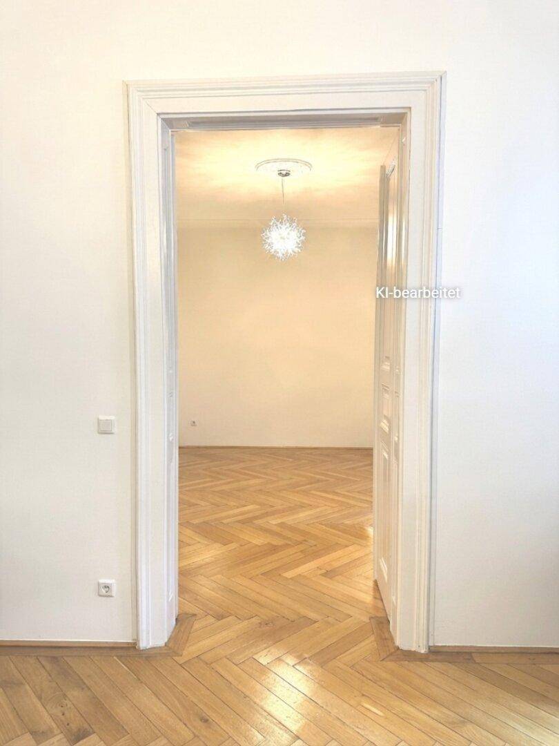 Blick durch eine hohe Türöffnung auf einen weiteren Raum mit Parkettboden und Deckenleuchte.