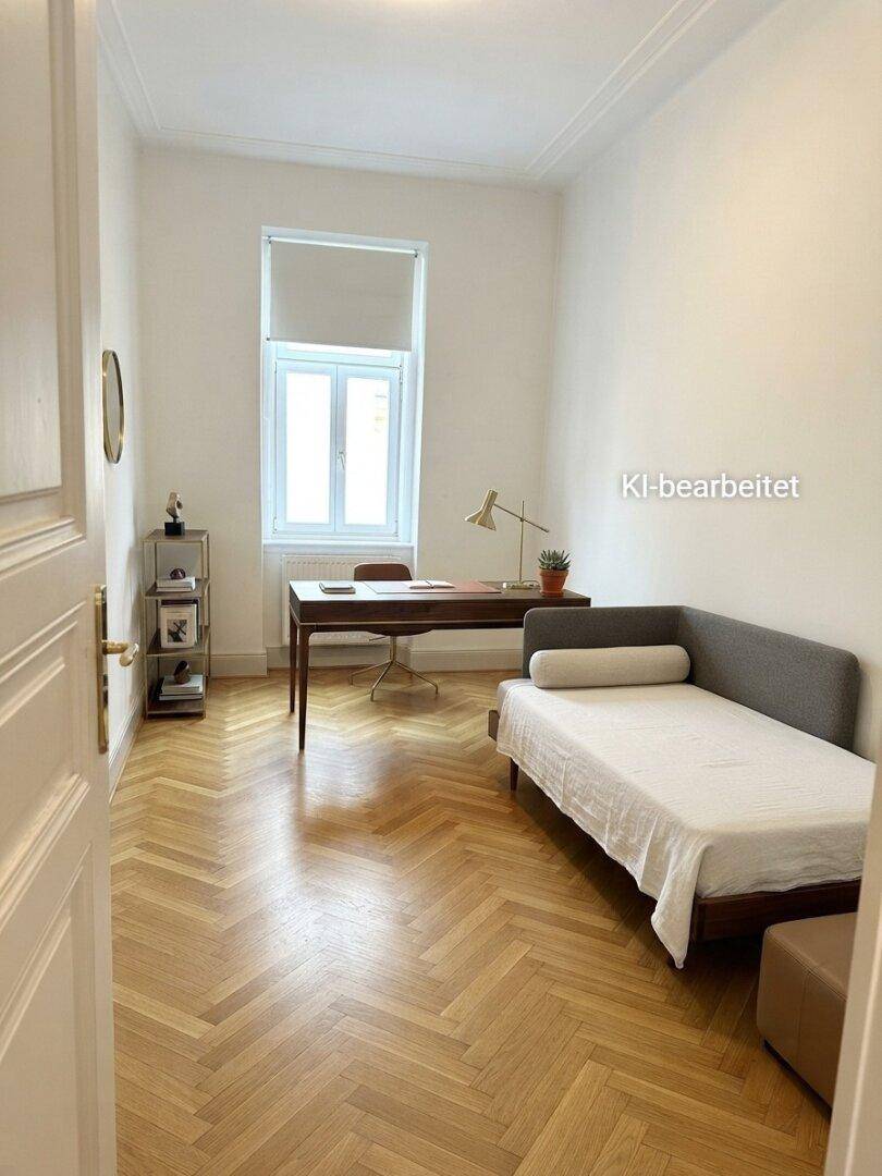 Ruhiges Arbeitszimmer mit Schreibtisch, Tagesbett, Parkettboden und einem großen Fenster.