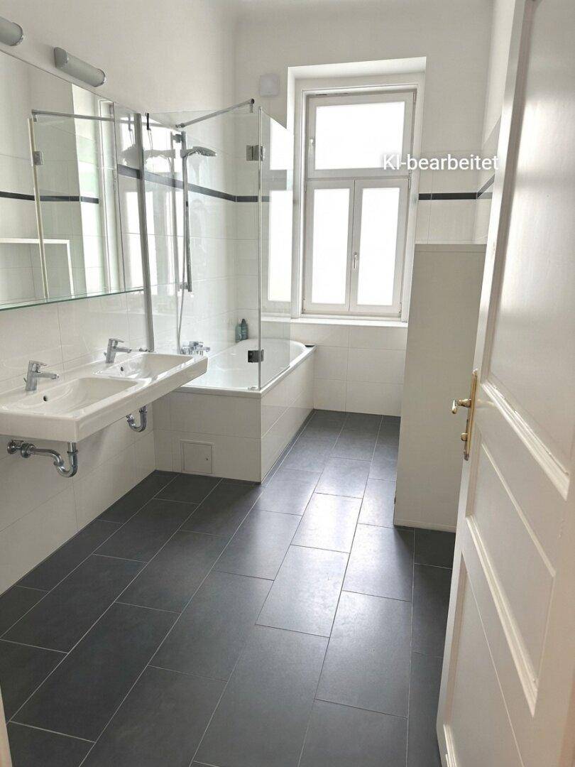 Helles Badezimmer mit Badewanne, Doppelwaschbecken, Dusche und dunklen Bodenfliesen.