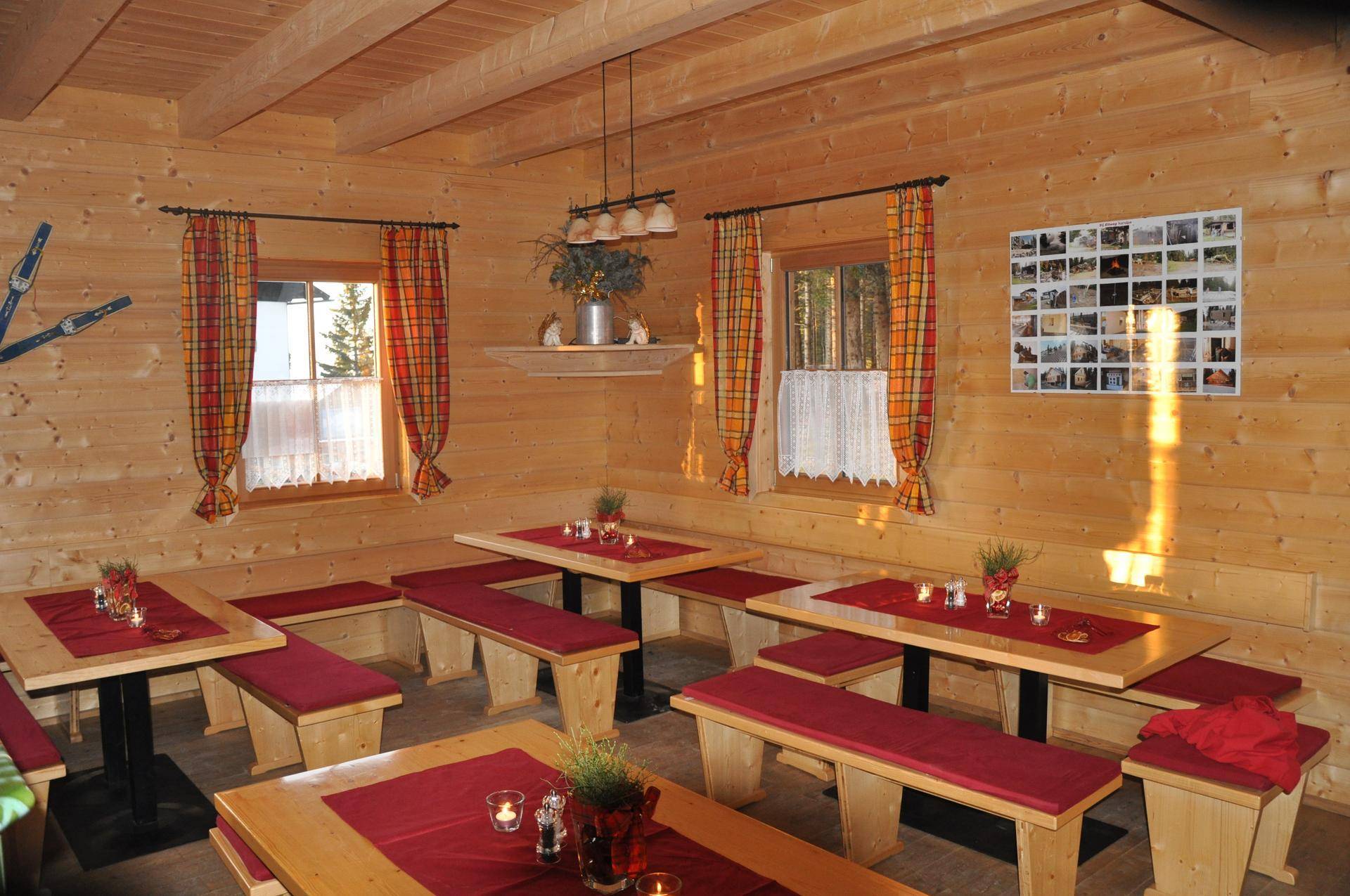 Gemütlicher Essbereich in einer Holzhütte mit Holztischen, Bänken und karierten Vorhängen, hell beleuchtet.