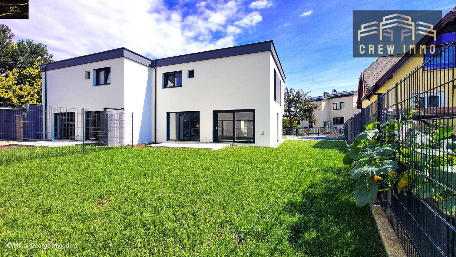 Rückseite eines modernen Hauses mit großem Garten und bodentiefen Fenstern.
