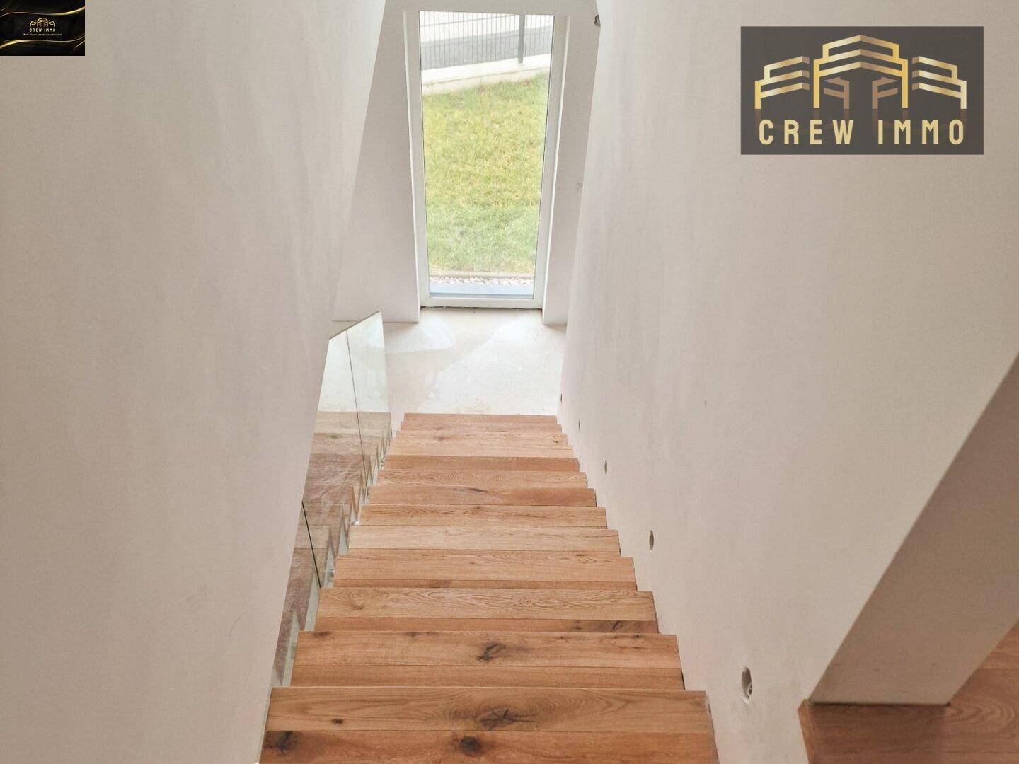 Elegante Holztreppe mit Glasgeländer, die in den unteren Bereich des Hauses führt.