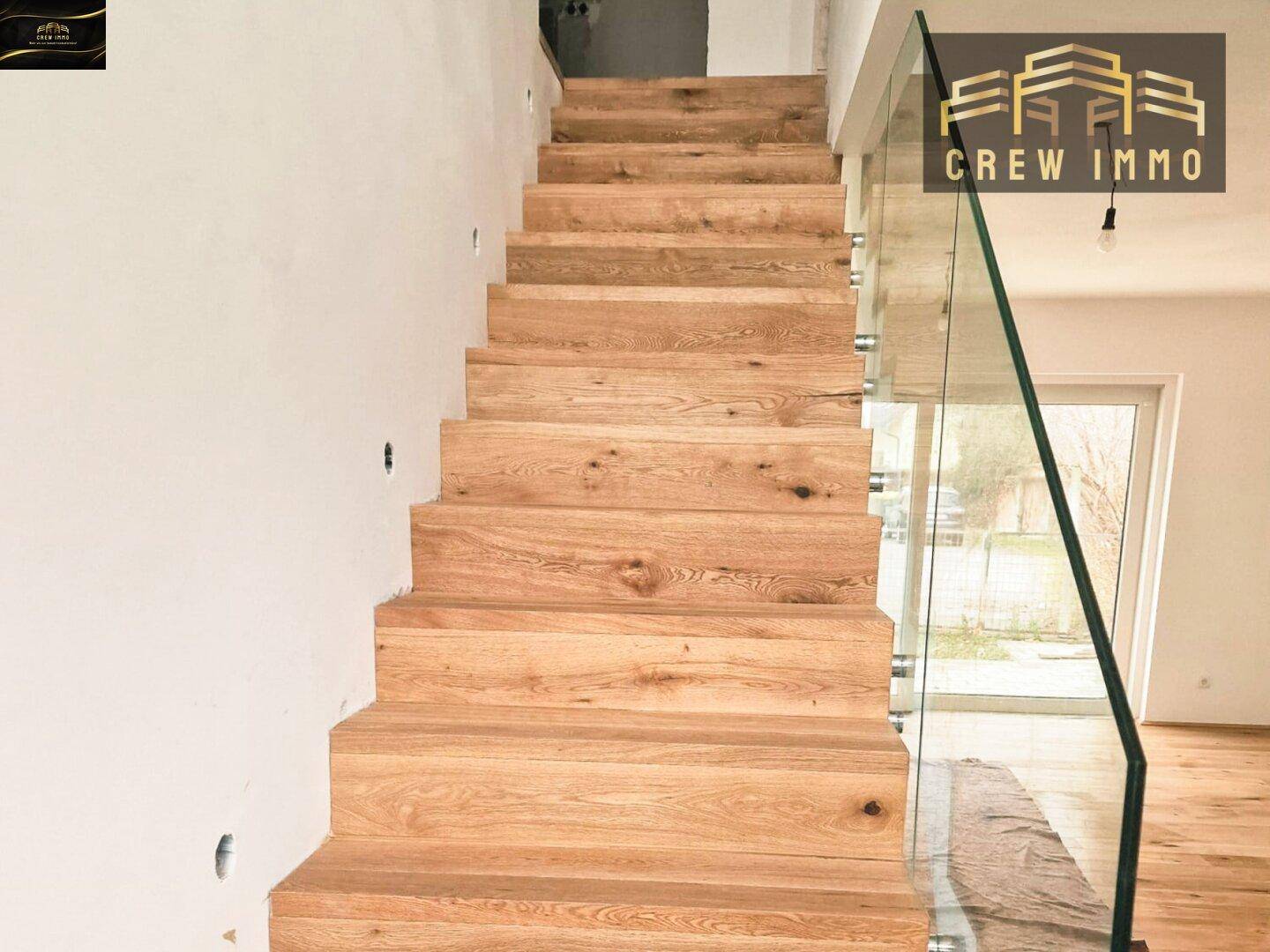 Moderne Holztreppe mit transparentem Glasgeländer, die die oberen Etagen verbindet.