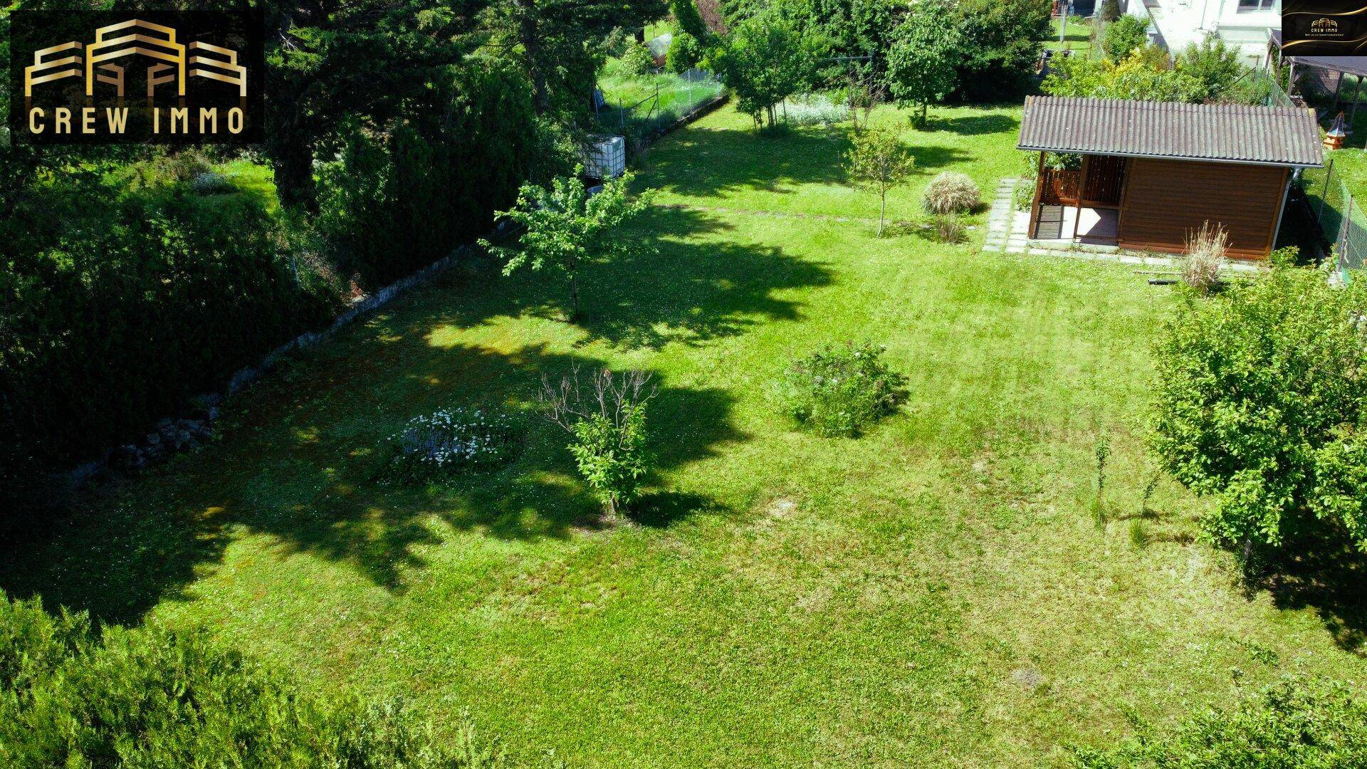 Großer, gepflegter Gartenbereich mit Rasenfläche und einem kleinen Gartenhaus im Hintergrund.