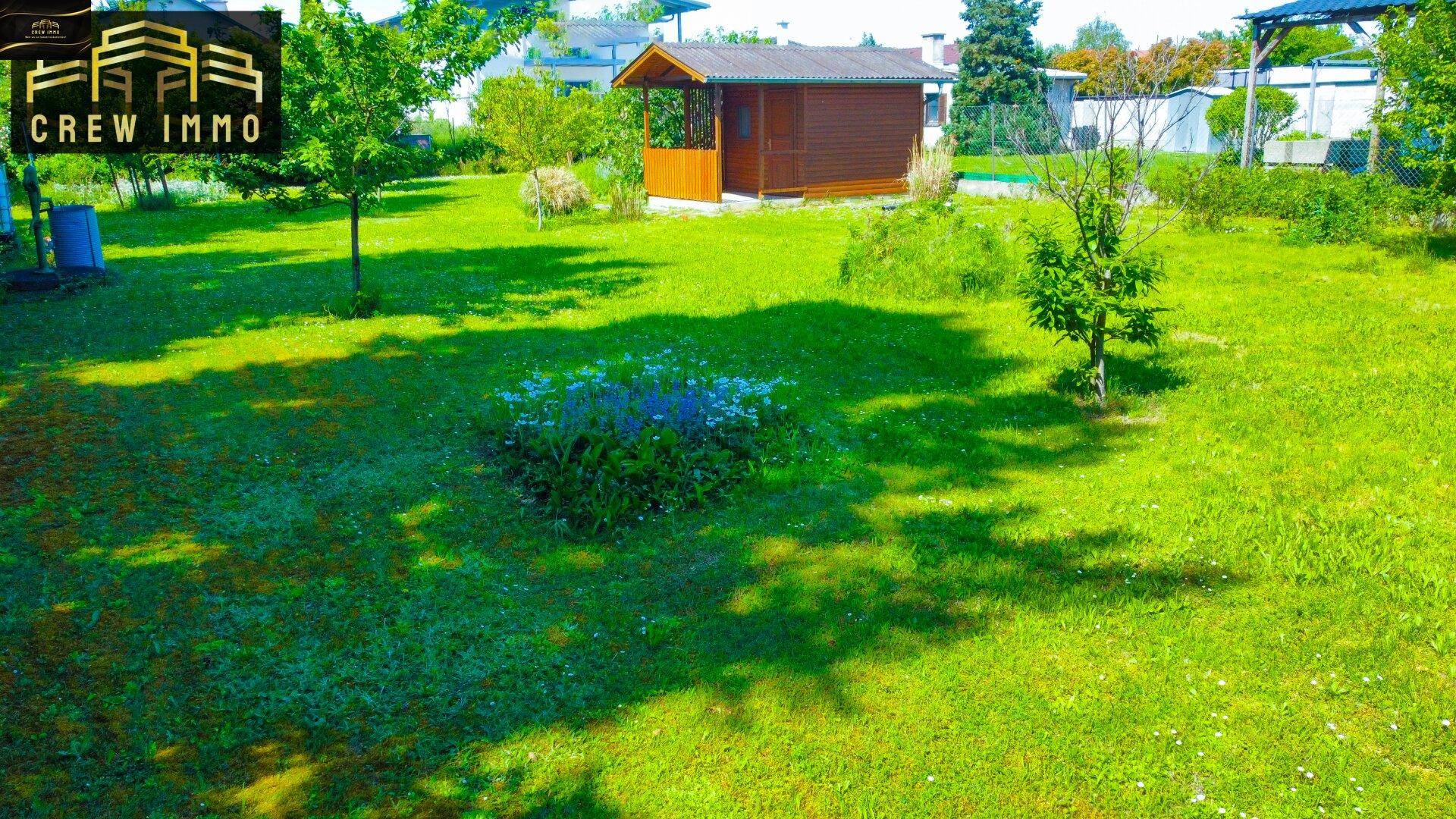 Gepflegter Garten mit Rasen, Blumenbeet und einer charmanten Gartenhütte im Hintergrund.