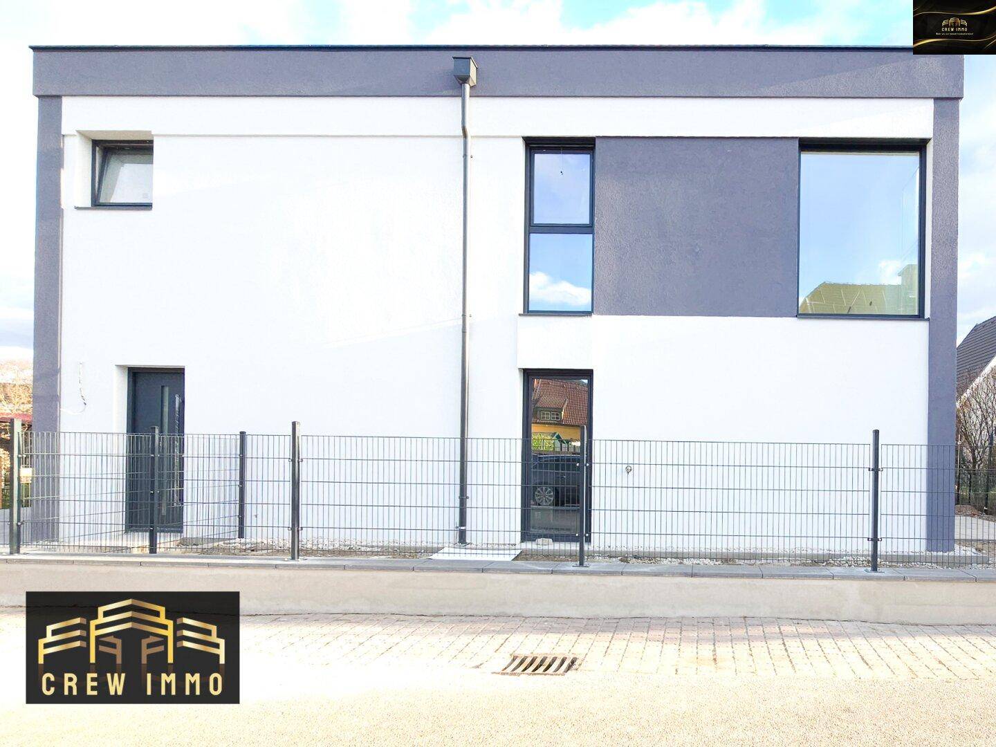 Vorderansicht des modernen Neubaus mit weißer und grauer Fassade, großen Fenstern und minimalistischem Design.