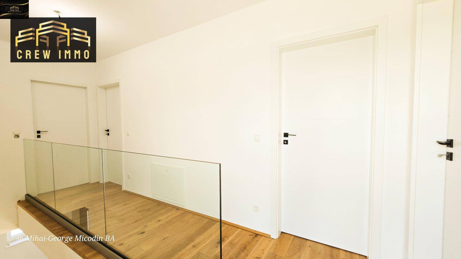 Heller Flur im Obergeschoss mit Holzboden, weißen Türen und moderner Glasbrüstung.