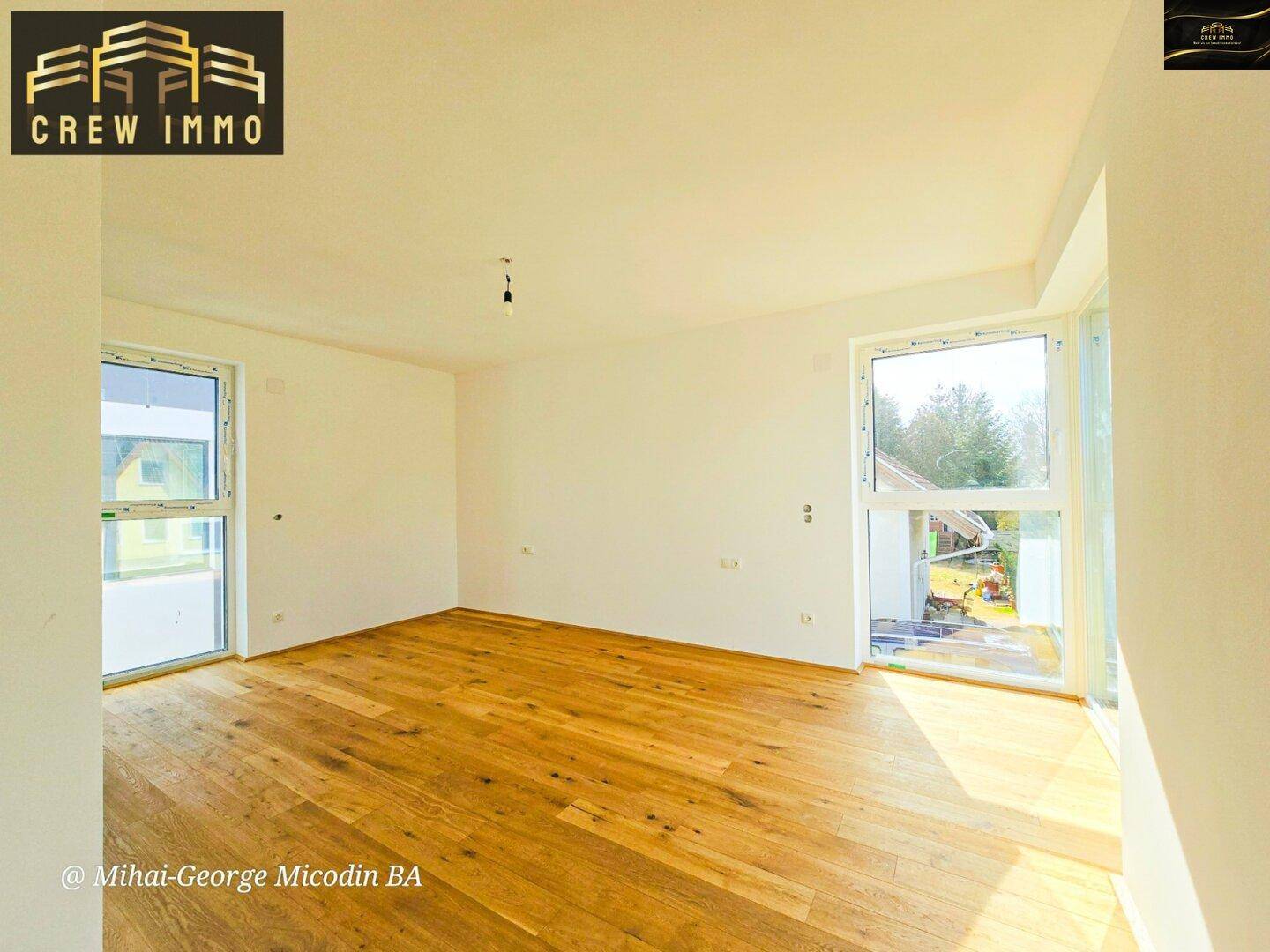 Helles Schlafzimmer mit Holzboden und großen Fenstern, die viel Tageslicht hereinlassen und eine grüne Aussicht bieten.