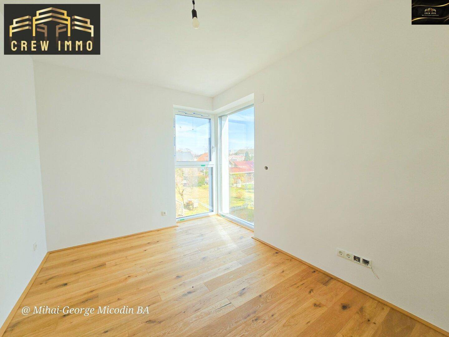 Geräumiges Schlafzimmer mit Holzboden und Eckfenstern für optimale Belichtung und eine weite Aussicht.