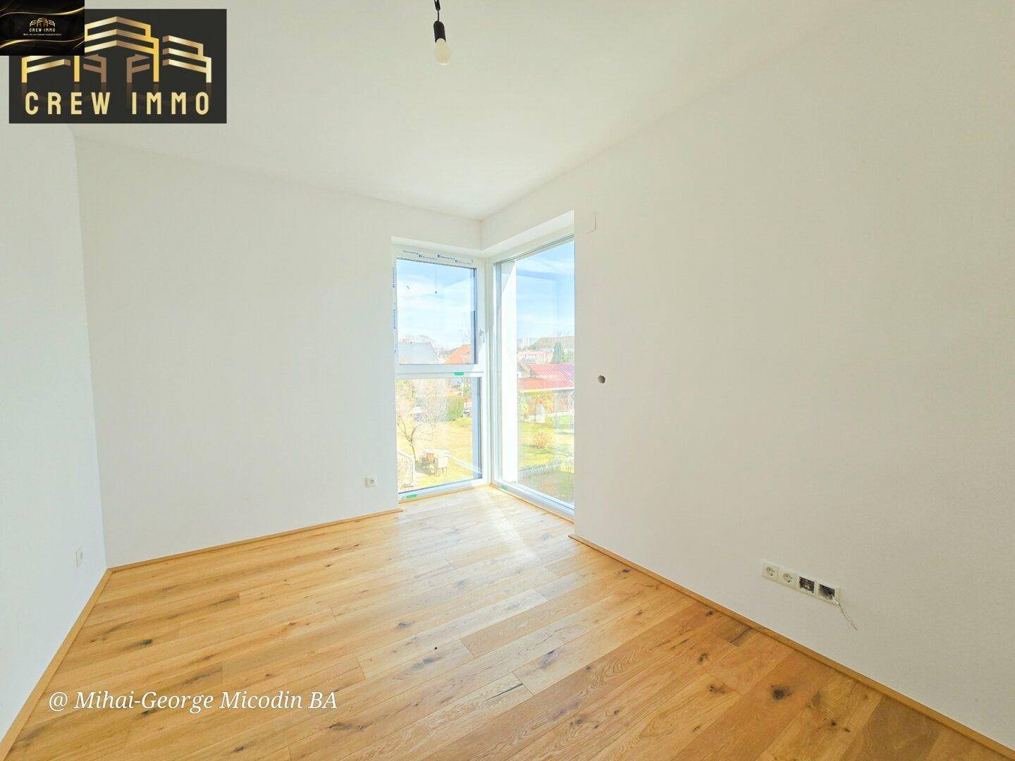 Helles Zimmer mit Eckfenstern und Holzboden, bietet viel Tageslicht und Ausblick.